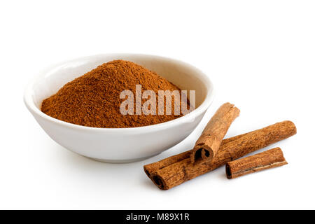Fein gemahlener Zimt in weißer Keramik Schüssel isoliert auf Weiss. Zimtstangen. Stockfoto