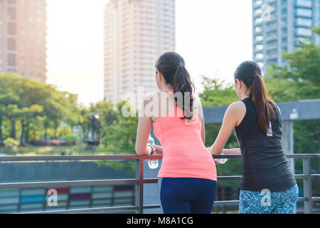 Asiatische Frau runner stützte sich auf einen Zaun in Pause, Trinkwasser nach dem Ausführen im Stadtzentrum. Gewichtsverlust, Fitness und gesunde Lebensweise. Stockfoto