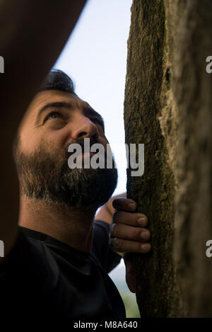 Jungen Erwachsenen aktiven Mann klettern eine Felswand in sonnigen Sommertag auf dem Berg outdoor. Stockfoto