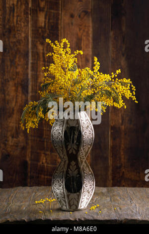 Ein Bouquet von Mimosa in einem exquisiten Vase. Still-life auf einem hölzernen Hintergrund. Stockfoto