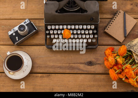 Obere Ansicht Schuß eines retro Schreibmaschine, Tasse Kaffee, orange Ranunkeln, vintage Film Kamera, Notepad mit schwarzem Stift auf rustikalen Holzmöbeln Hintergrund. Cop Stockfoto