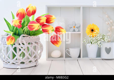 Weißer Tisch mit roten und gelben Tulpen und Frühling Dekorationen in Weiß Warner Stockfoto