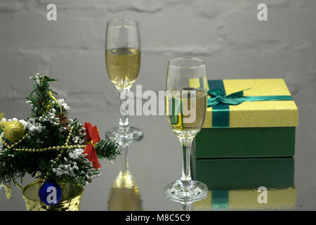 Zwei Gläser mit Sekt, Fir Tree Branch mit Dekoration, Geschenkboxen auf einem schwarzen Hintergrund mit mehrfarbigen lightes von Garland. Neues Jahr und Chri Stockfoto