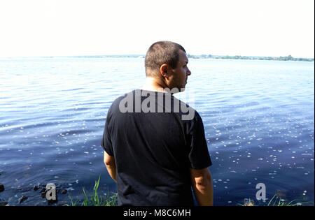 Profil der bärtige Mann auf dem Fluss Hintergrund. Junge Kerl, genießen Sie die frische Luft, stehend auf dem Wasser Bank. Ruhe, Entspannung, Genuss, Natur Konzept Stockfoto