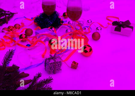 Weihnachtsdekoration mit Schneeflocken, Kerzen, ein grüner Zweig und roten Wein in Gläsern rosa Hintergrund Stockfoto