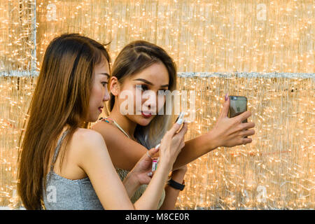 Zwei hübsche vietnamesischen Mädchen nehmen eine selfie mithilfe Ihres Smartphones vor einer Mauer der Lichter, Ho Chi Minh City, Saigon, Vietnam Stockfoto