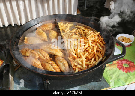 Straße fast food - Pommes frites und gebratenem Rindfleisch und Huhn Kuchen auf einer großen Pfanne. Feder sonnigen Tag Außenaufnahme Stockfoto