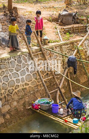 Kinder beobachten Frau Wäsche waschen in Inle Lake, in der Nähe von Indein Dorf, Shan Staat, Myanmar (Burma), Asien im Februar - Alltag Lebensstil Stockfoto