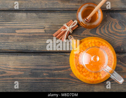 Sanddorn Tee in einem transparenten Teekanne mit Honig auf Holztisch. Traditionelle Herbst trinken. Im rustikalen Stil. Selektive konzentrieren. Platz kopieren Stockfoto