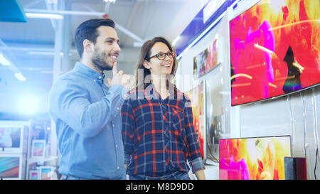 Junges Paar Einkaufen für eine Neue 4K-TV in der Unterhaltungselektronik. Sie versuchen, auf das beste Modell zu entscheiden, aber Zweifel. Stockfoto