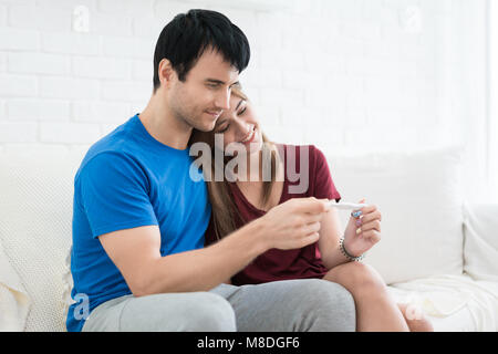 Nahaufnahme der glückliche junge Frau, die man nach dem positiven Schwangerschaftstest sitzen neben Mann im Zimmer Stockfoto