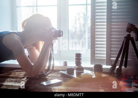 Mitte der erwachsenen Frau, neben dem Fenster, Kamera, Kamera Objektive auf Tisch vor ihr Stockfoto