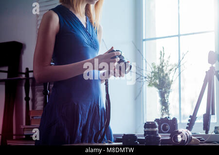 Mitte der erwachsenen Frau, neben dem Fenster, Kamera, Kamera Objektive auf den Tisch vor ihr, mittlere Partie Stockfoto
