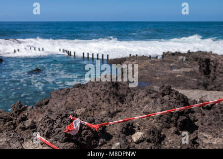 Rotes Klebeband über den Felsen, um zu verhindern, dass die Leute an der Küste, wo es sehr raue See brechen über Felsen und felsenpools an der Küste zu einem Stockfoto