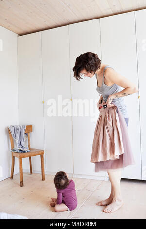 Mutter holding Rock wider sie, Baby Mädchen sitzen auf dem Boden gerade Ihre Stockfoto