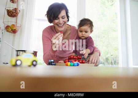Mutter Holding Baby Mädchen am Küchentisch, Haufen von Tomaten vor Ihnen Stockfoto