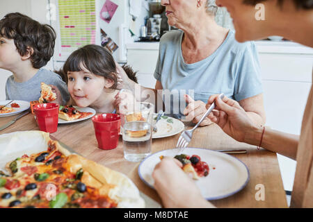 Drei generation Familie am Küchentisch sitzen essen Pizza Stockfoto