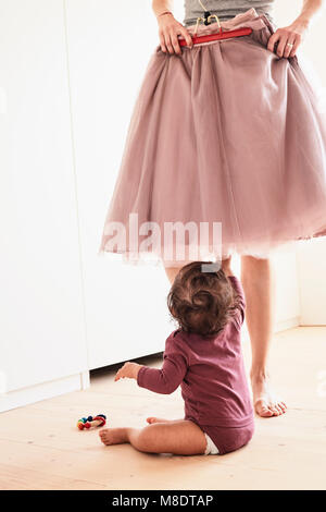 Mutter holding Rock wider sie, Baby Mädchen sitzen auf dem Boden beobachtete, geringe Abschnitt Stockfoto