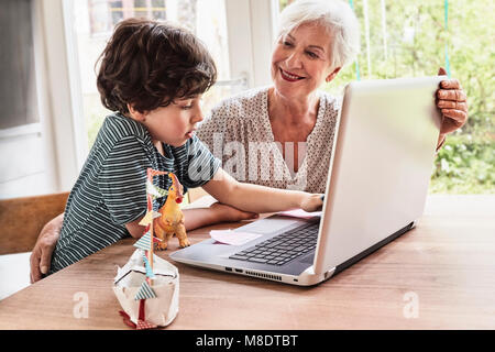 Großmutter und Enkel am Tisch sitzen, mit Laptop Stockfoto