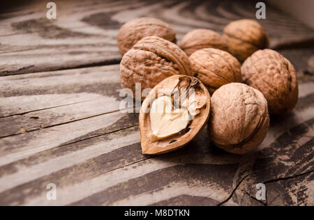 Walnüsse auf einem grauen texturierte Holztisch. Sortiment von Muttern auf urigen alten Holz- Hintergrund und zersplitterte Nussbaum mit Herz isoliert-förmigen Kern. Stockfoto