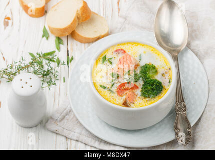 Fischsuppe mit Kartoffeln, Karotten, Tomaten und Brokkoli in einer weißen Schüssel auf hellem Holztisch Stockfoto