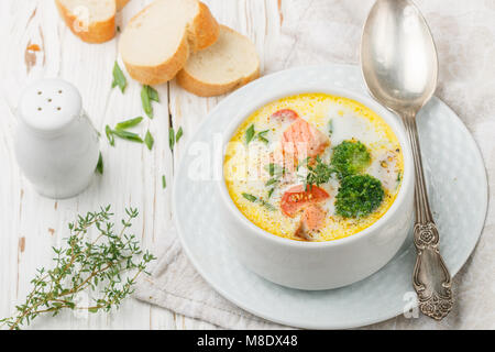 Chowder mit Forellen und Gemüse - Kartoffeln, Karotten, Tomaten und Brokkoli in einer weißen Schüssel auf hellem Holztisch Stockfoto