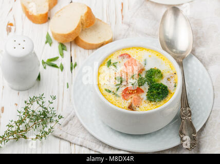 Fischsuppe mit Kartoffeln, Karotten, Tomaten und Brokkoli in einer weißen Schüssel auf hellem Holztisch Stockfoto