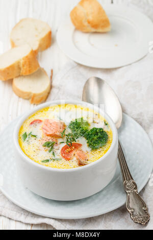 Chowder mit Lachs, Kartoffeln, Karotten, Tomaten und Brokkoli in einer weißen Schüssel auf hellem Holztisch Stockfoto