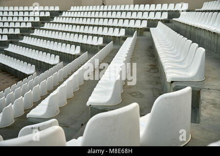 Gerade Reihen moderner Stühle aus weißem Kunststoff an bequemen Zuschauerplätzen eines großen Stadions bei hellem Licht Stockfoto