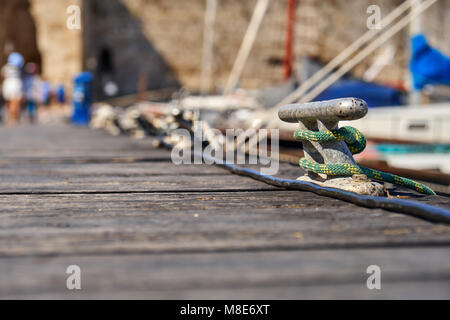 Metallfestlegeplatz mit Seil auf hölzernen Pier am blauen Meerwasser unter hellem Sonnenlicht am Sommertag aus der Nähe Stockfoto