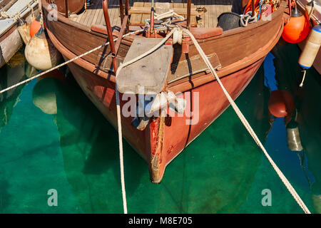 Hölzerne Motorboote, die mit Seilen auf blauem Meerwasser am Pier festgemacht sind und das helle Sonnenlicht am Sommertag aus der Nähe reflektieren Stockfoto