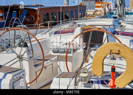 Weißes, glänzendes Motorboot mit modernem Design, das am Pier mit Seilen auf blauem Meerwasser festgemacht ist, das am Sommertag helles Sonnenlicht reflektiert Stockfoto