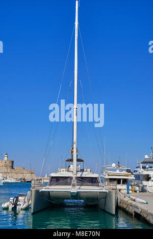 Weißes, glänzendes Katamaran-Boot im modernen Design, das am Pier mit Seilen auf blauem Meerwasser vertäut ist und am Sommertag helles Sonnenlicht reflektiert Stockfoto