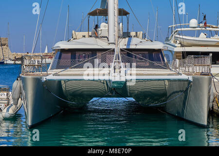 Weißes, glänzendes Katamaran-Boot im modernen Design, das am Pier mit Seilen auf blauem Meerwasser vertäut ist und am Sommertag helles Sonnenlicht aus der Nähe reflektiert Stockfoto