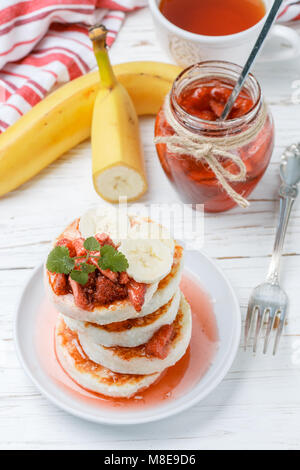 Hausgemachten Quark Pfannkuchen mit Erdbeermarmelade und eine Banane. Syrniki. Traditionelle schmackhaftes und gesundes Frühstück. Selektiver Fokus Stockfoto