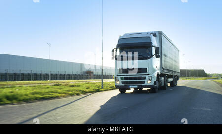 Front-View Semi Truck mit Cargo Trailer Fahren auf einer Landstraße. Er beschleunigt durch industrielle Lagerbereich während die Sonne scheint Stockfoto