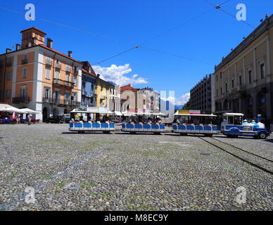 LOCARNO, SCHWEIZ EUROPA Juli 2017: kleiner touristischer Zug, farbenfrohe Gebäude an der Piazza Grande Hauptplatz der Stadt mit Bars, Restaurants, Straßenbahn tr Stockfoto