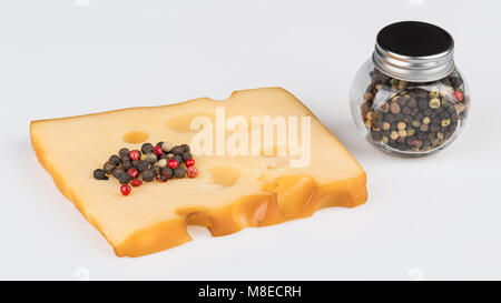 Stück Hartkäse mit einem Stapel von bunte Pfefferkörner. Klumpen von geräuchertem Emmental mit Löchern und einem Spice jar mit Pfefferkörnern auf weißem Hintergrund. Stockfoto