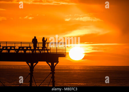 Aberystwyth Wales UK, Freitag, 16. März 2018 Deutschland Wetter: Am Ende eines milden Frühling Nachmittag, ein junges Paar sind in Silhouette am Ende des Piers gefangen wie die Sonne spektakulär über die Cardigan Bay setzt auf aberystwyth an der Westküste von Wales das Met Office hat eine Reihe von Gelb und Gelb Warnungen für Schnee und Eis für das Wochenende, als Blast sehr kalte Luft bläst in aus dem Osten Foto © Keith Morris/Alamy leben Nachrichten Stockfoto