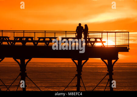 Aberystwyth Wales UK, Freitag, 16. März 2018 Deutschland Wetter: Am Ende eines milden Frühling Nachmittag, ein junges Paar sind in Silhouette am Ende des Piers gefangen wie die Sonne spektakulär über die Cardigan Bay setzt auf aberystwyth an der Westküste von Wales das Met Office hat eine Reihe von Gelb und Gelb Warnungen für Schnee und Eis für das Wochenende, als Blast sehr kalte Luft bläst in aus dem Osten Foto © Keith Morris/Alamy leben Nachrichten Stockfoto