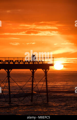 Aberystwyth Wales UK, Freitag, 16. März 2018 Deutschland Wetter: Am Ende eines milden Frühling Nachmittag, ein junges Paar sind in Silhouette am Ende des Piers gefangen wie die Sonne spektakulär über die Cardigan Bay setzt auf aberystwyth an der Westküste von Wales das Met Office hat eine Reihe von Gelb und Gelb Warnungen für Schnee und Eis für das Wochenende, als Blast sehr kalte Luft bläst in aus dem Osten Foto © Keith Morris/Alamy leben Nachrichten Stockfoto