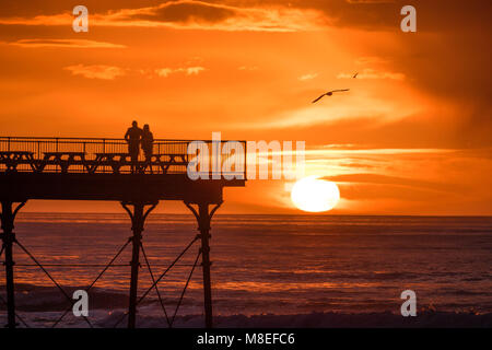 Aberystwyth Wales UK, Freitag, 16. März 2018 Deutschland Wetter: Am Ende eines milden Frühling Nachmittag, ein junges Paar sind in Silhouette am Ende des Piers gefangen wie die Sonne spektakulär über die Cardigan Bay setzt auf aberystwyth an der Westküste von Wales das Met Office hat eine Reihe von Gelb und Gelb Warnungen für Schnee und Eis für das Wochenende, als Blast sehr kalte Luft bläst in aus dem Osten Foto © Keith Morris/Alamy leben Nachrichten Stockfoto