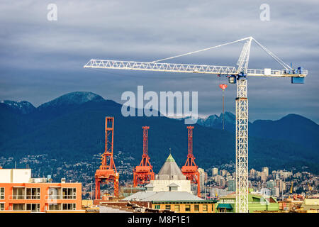 Das Gebäude tower crane Türme über eine moderne Stadt mit hohen Gebäuden und über Berge mit Wald bedeckt, der blauen Wolken im Hintergrund Stockfoto