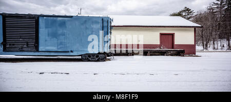 Ein Vintage alten Bahnhof box car auf einem Abstellgleis geparkt neben einem alten Fracht- Haus im Schnee. Stockfoto