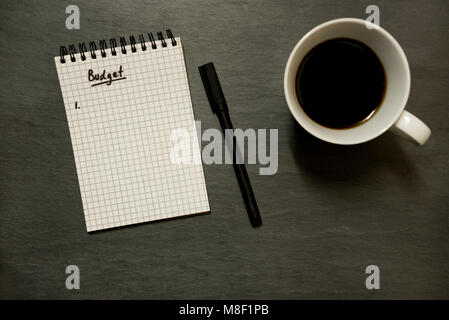 Haushalt Liste in vermaschten Spirale Notizblock mit Stift und Tasse Kaffee, auf schiefer Table Top - von oben, minimale Stockfoto