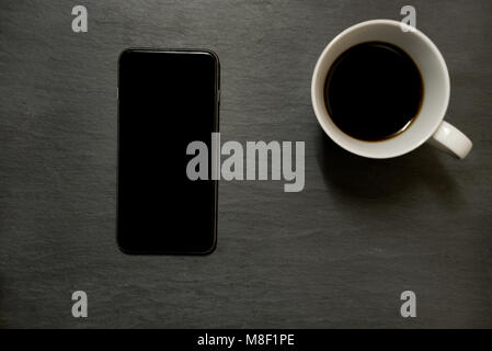 Handy / Smartphone und Tasse Kaffee - von oben auf dunklem Schiefer table top Hintergrund, mit Kopie Raum Stockfoto