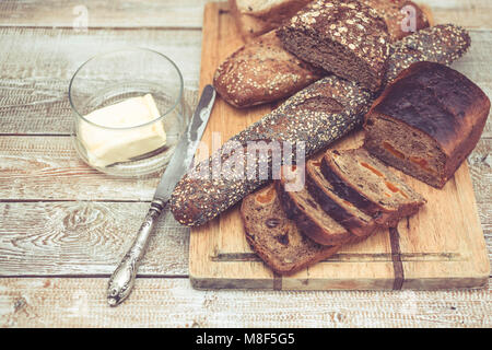 Verschiedene von Weizen und Roggen Brot auf ein Schneidebrett. Brot, Messer und Butter. Gesundes Frühstück Konzept. Einfach Muskelaufbau. Holz- Hintergrund Stockfoto