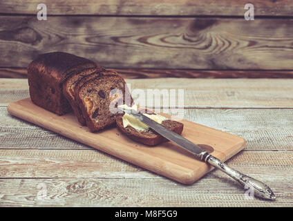 Dunkle Roggenbrot mit getrockneten Aprikosen und Rosinen. Gesundes Brot. Scheiben, Tabelle Messer und Butter. Holz- Hintergrund Stockfoto