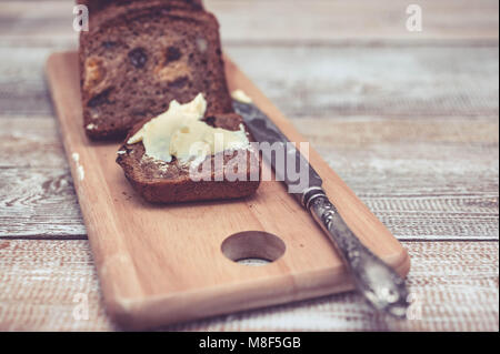 Dunkle Roggenbrot mit getrockneten Aprikosen und Rosinen. Gesundes Brot. Scheiben, Tabelle Messer und Butter. Holz- Hintergrund Stockfoto