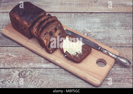 Dunkle Roggenbrot mit getrockneten Aprikosen und Rosinen. Gesundes Brot. Scheiben, Tabelle Messer und Butter. Holz- Hintergrund Stockfoto